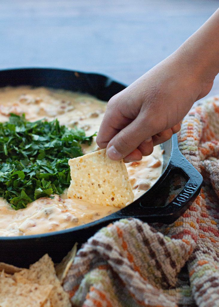 hand-dipping-into-a-pot-of-dairy-free-sausage-queso-dip-seen-from-above