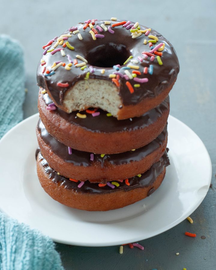 four-gluten-free-donuts-stacked-on-top-of-each-other-with-a-bite-taken-out-covered-in-chocolate-frosting-and-sprinkles