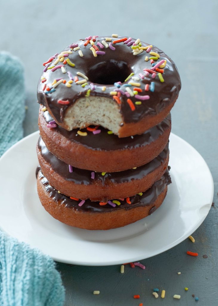 four-gluten-free-donuts-stacked-on-top-of-each-other-with-a-bite-taken-out-covered-in-chocolate-frosting-and-sprinkles