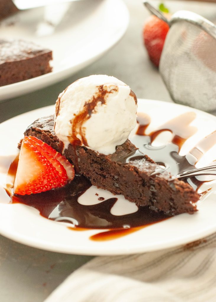 flourless-chocolate-torte-slice-side-angle-with-chocolate-sauce-and-vanilla-ice-cream-on-top