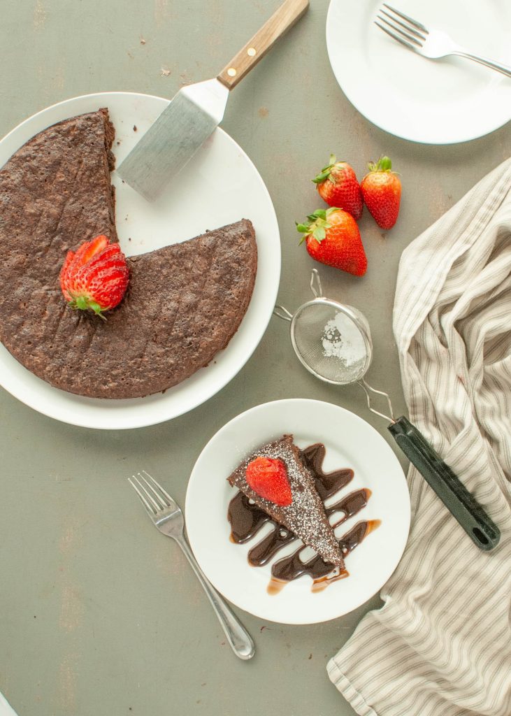 flourless-chocolate-torte-with-one-slice-on-a-plate-rest-of-cake-in-the-pan-shot-from-above-with-strawberries