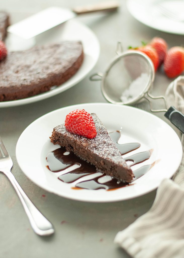 flourless-chocolate-tort-eslice-sitting-on-top-of-chocolate-sauce-with-strawberry-on-top