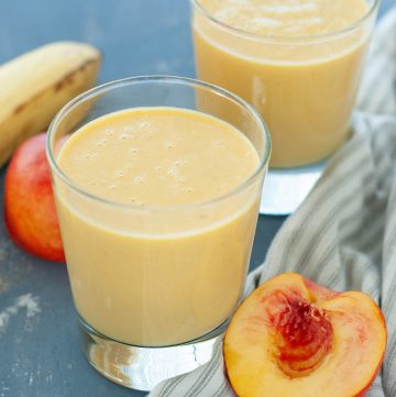 dairy-free peach protein smoothie in two glasses with fruit around it