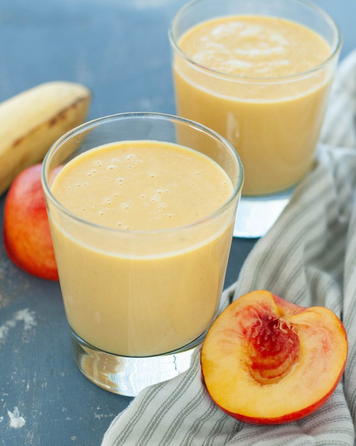 dairy-free peach protein smoothie in two glasses with fruit around it