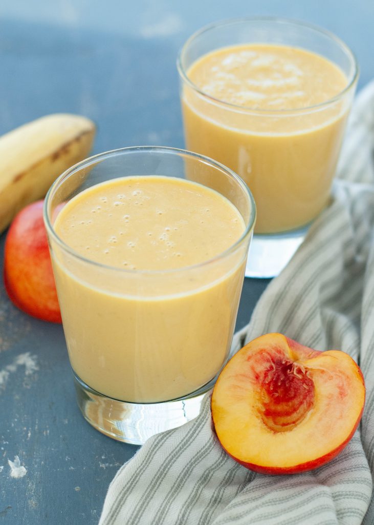 dairy-free peach protein smoothie in two glasses with fruit around it
