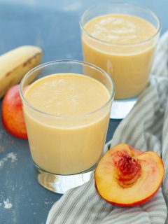 dairy-free peach protein smoothie in two glasses with fruit around it